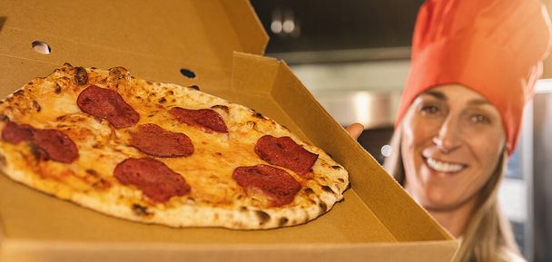 panadero de pizza hembra sosteniendo una pizza salami fresca del horno de piedra en una caja para la entrega en la pizzería italiana, tamaño de la pancarta - Foto, imagen