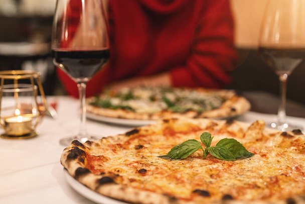 mensen die rode wijn drinken en margherita pizza eten met basilicum  - Foto, afbeelding