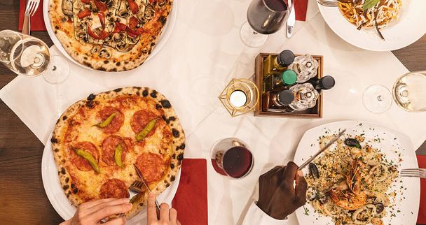 amigos comiendo pasta, pizza y vino - personas comiendo en el restaurante - Enfoque en la mesa central - Estilo de vida de verano, comida y concepto de amistad - Foto, Imagen