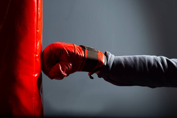 Gyakorolni az ütéseket egy bokszzsákon a tornateremben. Az előtérben egy piros kesztyű és egy piros bokszzsák.. - Fotó, kép