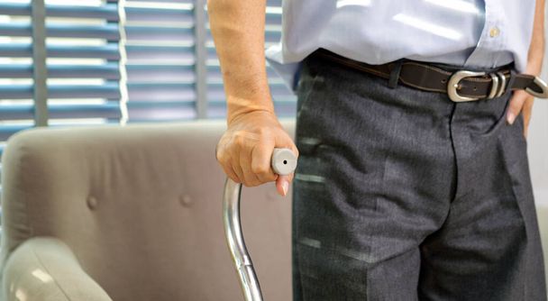 Close up hand of elderly man using walking stick trying to stand and walk at home, Senior man with health problems using walking stick to walk at home - Photo, Image