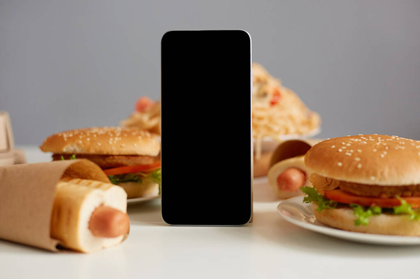 Image of table with different fast food and smart phone with balck blank screen, copy space for advertisement of fast food restaurant, mockup, advertisemet area for promotion, - Foto, imagen