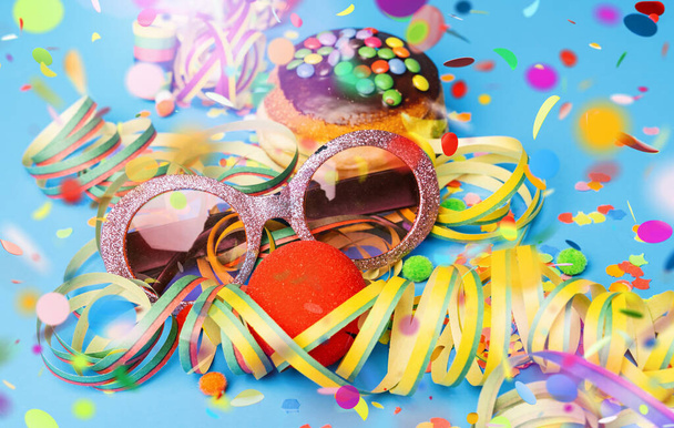 Karnevalssonnenbrille mit Donut aus Deutschland mit Puderschokoladenzucker auf blauer Fläche mit Konfetti und Luftschlangen darauf - Hintergrund für eine Karnevalsparty oder Partys - Foto, Bild