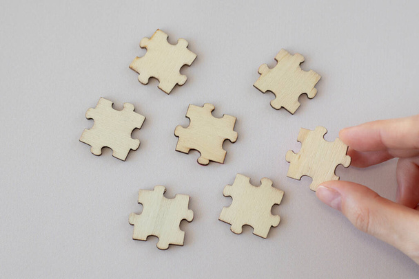 Una mano femminile tiene un puzzle di legno accanto ad altri sparsi su uno sfondo beige. Falsificazione. - Foto, immagini