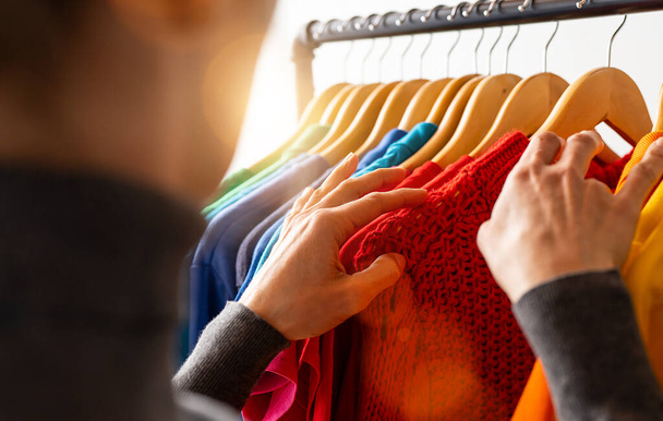 Fashion clothes hanging on clothing rack, in colorful rainbow colors selection of clothes closet. Woman choose outfits on hangers in store closet. LGBT colors - Φωτογραφία, εικόνα
