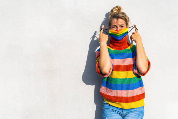Молода жінка знімала маску на обличчі геїв під час пандемії Коронавірусу в кольорах веселки символ образу соціального руху Lgbtq, з авторським простором для вашого індивідуального тексту. - Фото, зображення