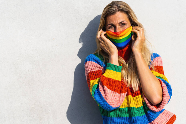 Молодая женщина надела маску для лица на гей-парад во время пандемии коронавируса в радужных цветах - символ концепции социального движения Lgbtq, с копирайтом для вашего индивидуального текста. - Фото, изображение
