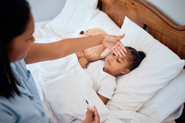 Θερμόμετρο, πυρετός και μαμά με άρρωστο κορίτσι ξαπλωμένη στο κρεβάτι, αγγίζοντας το μέτωπο για να αισθανθείτε τη θερμοκρασία του σώματος. Οικογένεια, υγειονομική περίθαλψη και μητέρα με μικρό παιδί στο υπνοδωμάτιο με κρυολόγημα, γρίπη και τα συμπτώματα covid στο σπίτι. - Φωτογραφία, εικόνα