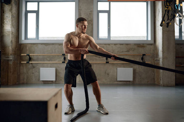 A strong man pulling training sports rope front view. Male athlete doing workout exercises at gym - Foto, Imagem