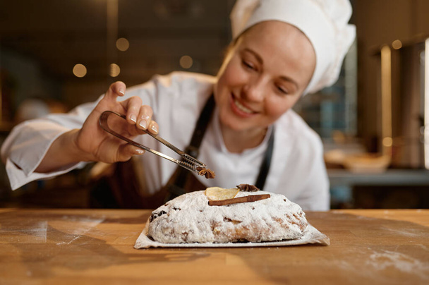 Kenyér pékség dolgozó visel egyenruha és kötény díszítő diéta búza kenyér vagy zsemle, miközben áll a modern konyhában - Fotó, kép