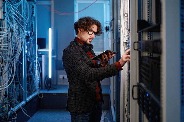 Young male IT master with digital tablet checking computer server configuration. Modern data center - 写真・画像