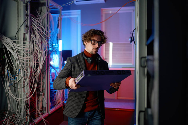 Portret van een specialist die hardware component in de hand houdt in de serverruimte. Supercomputer upgrade of reparatie concept - Foto, afbeelding