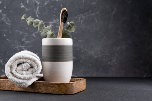 Eco friendly bathroom concept, sustainable lifestyle. Bamboo toothbrush in a glass with white towel and eucalyptus on wooden tray - Fotografie, Obrázek