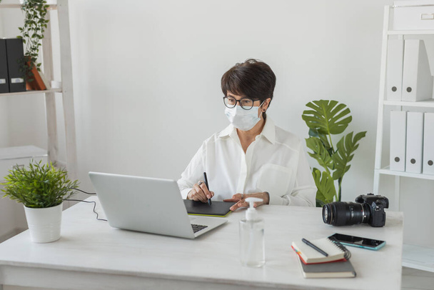 Mulher de meia-idade designer gráfico ou fotógrafo usando tablet gráfico digital enquanto trabalhava no escritório moderno, retocador feminino profissional sentado no espaço de trabalho moderno, tablet design genérico e - Foto, Imagem