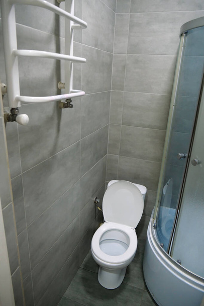 Cuarto de baño interior con inodoro blanco, toallero con calefacción, cabina de ducha y azulejos grises - Foto, imagen