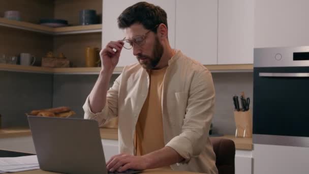 Biały mężczyzna pracujący na laptopie w kuchni cierpi z powodu ujęcia okularów z oczu. Zmęczony mężczyzna freelancer biznesmen praca z komputerem w domu czuć ból oczu dyskomfort z okularów wyczerpany wzrok - Materiał filmowy, wideo