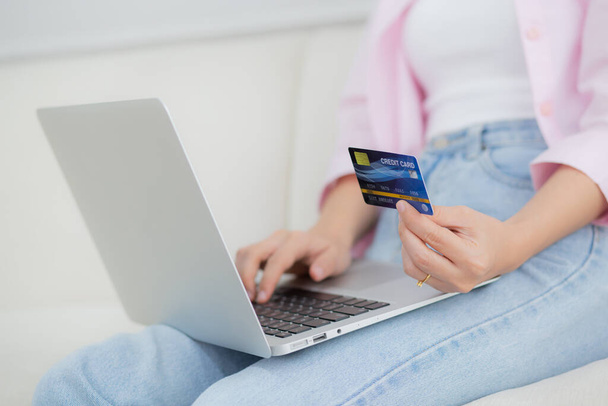 Closeup hands of woman sitting on sofa using laptop computer online shopping with credit card, happy female payment with debit card on couch, purchase and payment, business and technology concept. - Фото, изображение