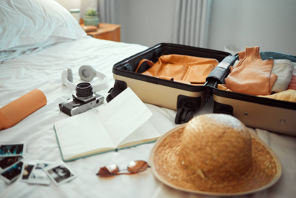Matka, matkatavarat ja makuuhuone matkalaukku, hattu ja kamera sängyllä hotellissa loman tai loman aikana. Vieraanvaraisuus, turisti ja lomakeskus matkatavaroiden kanssa huoneessa matkustamiseen tai nähtävyyksiin ulkomaille. - Valokuva, kuva