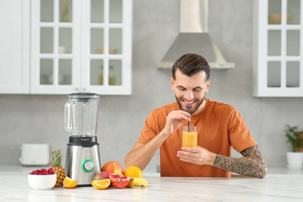 Handsome man with delicious smoothie at white marble table in kitchen - Фото, изображение