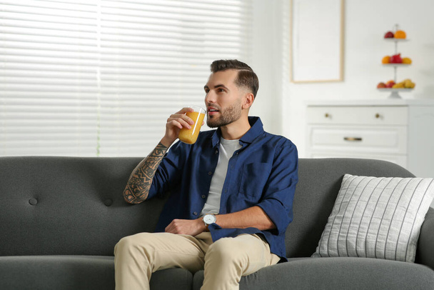Handsome man with delicious smoothie on sofa at home - Фото, изображение