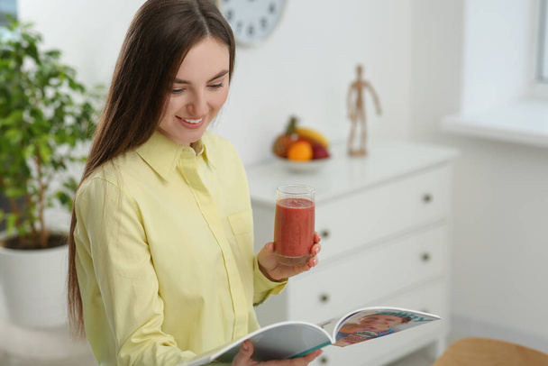 Beautiful young woman with delicious smoothie reading magazine at home. Space for text - Zdjęcie, obraz