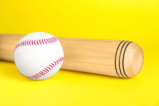 Wooden baseball bat and ball on yellow background, closeup. Sports equipment - Zdjęcie, obraz