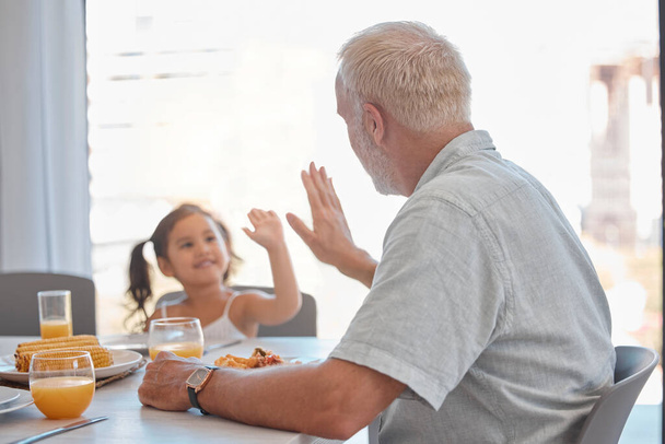 Pacsi, reggeli és család egy lánnyal és nagyapával, akik az ebédlőasztalnál ülnek, hogy egyenek. Motiváció, egészség és gyerekek egy idősebb férfival, aki arra ösztönzi unokáját, hogy egészségesen étkezzen. - Fotó, kép