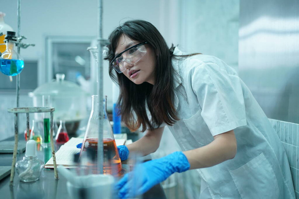 Wissenschaftler in Schutzkleidung entnimmt Probe und untersucht sie während des Experiments im Labor mit seinen Kollegen im Hintergrund - Foto, Bild