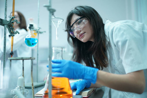 cientista no desgaste protetor que toma a amostra e a examina durante a experiência no laboratório com seus colegas no fundo - Foto, Imagem