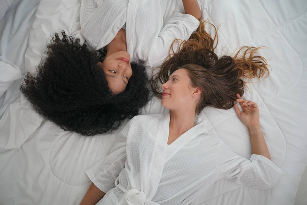 Female lesbian women looking at each other while lying down on bed in bedroom at home - Foto, Imagen
