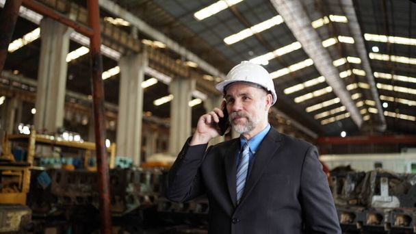 Fabrieksmanager of ondernemer in fabrieksmagazijn is in gesprek op mobiele telefoon. Achtergrond van het bedrijfsleven. - Foto, afbeelding