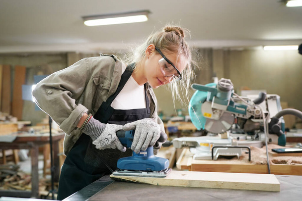 Νεαρή όμορφη γυναίκα που κάνει τη δουλειά της στο εργαστήριο ξυλουργός DIY. Ιδιοκτήτης μικρών επιχειρήσεων, νεαρή γυναίκα που εργάζεται στο εργοστάσιο επίπλων. - Φωτογραφία, εικόνα