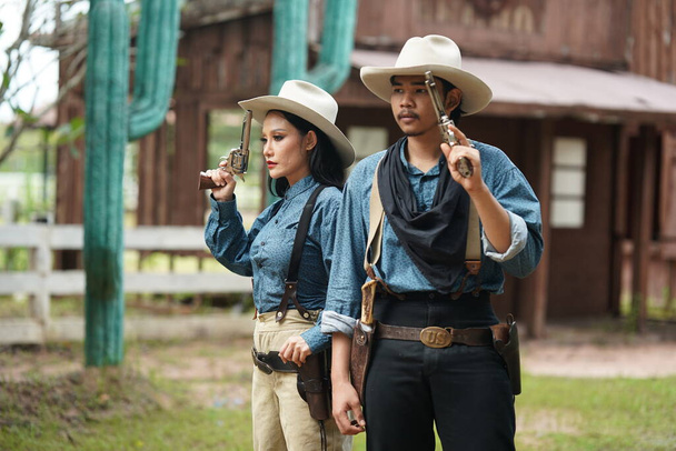 Brutální kovboj a kovbojka s revolvery na ranči. Lidé se zbraněmi, divoký západní životní styl - Fotografie, Obrázek