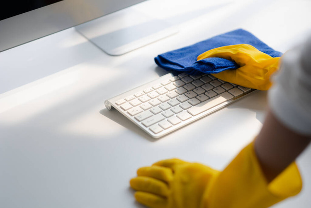 Person cleaning room, cleaning worker is using cloth to wipe computer keyboard in company office room. Cleaning staff. Concept of cleanliness in the organization. - 写真・画像
