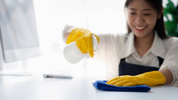 Odayı temizleyen kişi, temizlik personeli şirket ofisindeki masayı silmek için bez ve dezenfektan kullanıyor. Temizlik personeli. Organizasyondaki temizliği sürdürmek. - Fotoğraf, Görsel