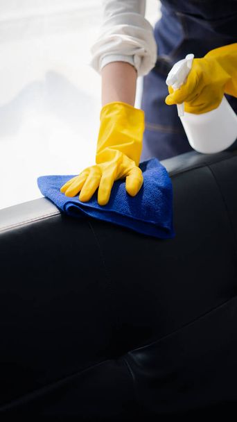 Osoba sprzątająca pokój, sprzątaczka używa tkaniny i środka dezynfekującego do wycierania kanap w biurze firmy. Sprzątacze. Utrzymanie czystości w organizacji. - Zdjęcie, obraz