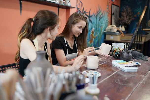 Handwerkerinnen sitzen am Tisch und arbeiten mit Tonvasen und Töpferhintergrund, Geschäftsinhaberin - Foto, Bild