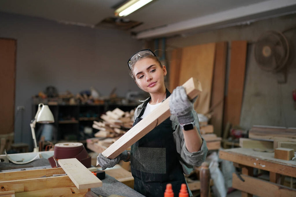 Junge schöne Frau bei der Arbeit in der Schreinerei DIY Werkstatt. Kleinunternehmerin, junge Frau, die in einer Möbelfabrik arbeitet. - Foto, Bild