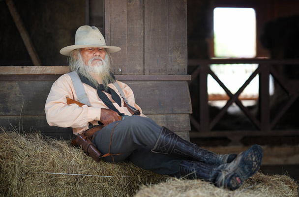 Surový kovboj s rukou na revolveru, texaský ranč na pozadí, západní - Fotografie, Obrázek