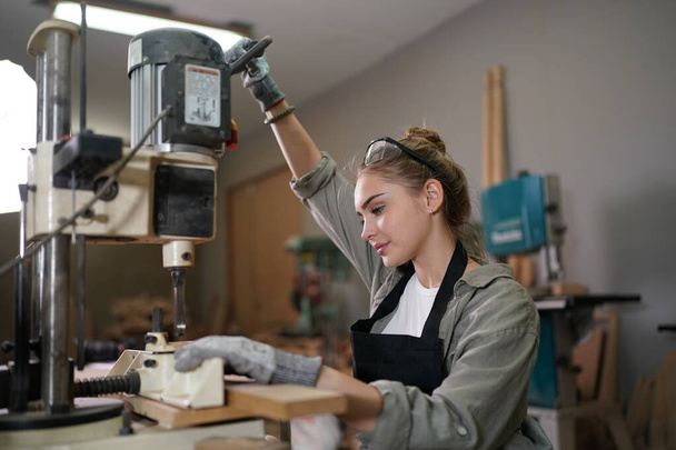 Young beautiful woman doing work in the carpenter DIY workshop room. Small Business owner, young woman who working at furniture factory. - Photo, Image