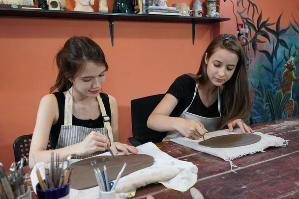 Artesanas sentadas a la mesa y trabajando con jarrones de barro y fondo de cerámica, propietaria de un negocio - Foto, imagen