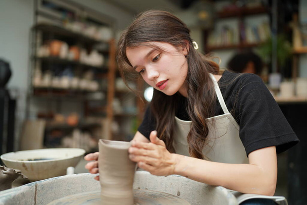 土船を形成しながら、陶器の車輪に座って、工芸品を使用してエプロンに集中した美しい職人のクローズアップ - 写真・画像