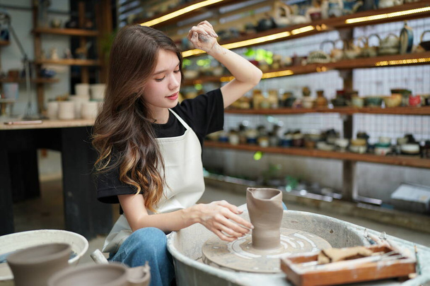 Primo piano di bella artigiana in grembiule seduta al negozio di ceramiche - Foto, immagini
