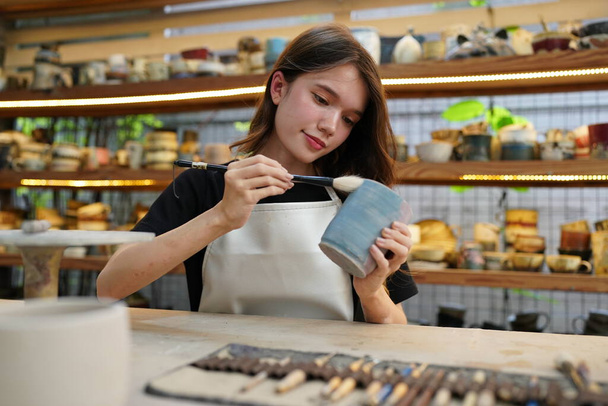 Primo piano di bella artigiana in grembiule seduta al negozio di ceramiche - Foto, immagini