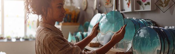Female decorator puts handmade epoxy resin tray on stand exposition in studio. High quality photo - Φωτογραφία, εικόνα
