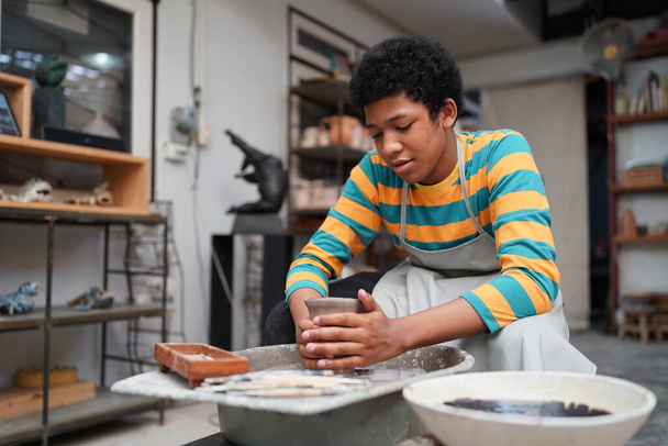Giovane afro adolescente mano vasaio rendendo vaso di argilla in laboratorio di ceramica - Foto, immagini