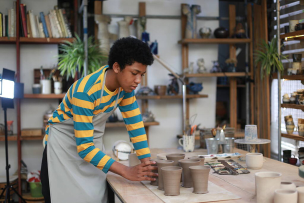 Young Afro teenager hand potter making clay vase in pottery workshop - Foto, immagini
