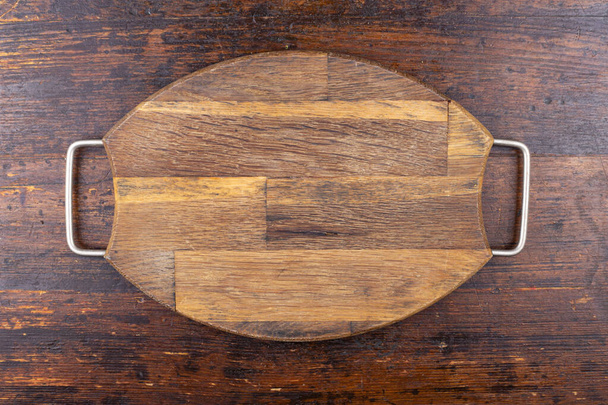 Wooden cutting board, oval, vintage, with iron handles on a wooden background. View from above - Photo, image