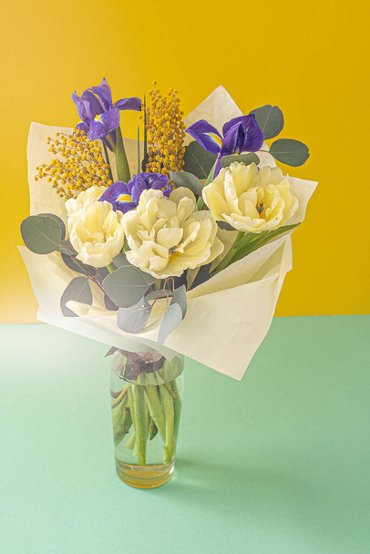 Spring bouquet of flowers. Irises, tulips, mimosa and eucalyptus. Yellow and blue flower. Bud close-up. Floral background. Purple iris, white double tulip. Gift. March mood. - 写真・画像