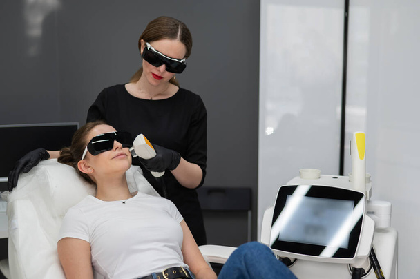 A woman on a couch in goggles undergoing a photorejuvenation procedure. Hardware cosmetology - Fotografie, Obrázek